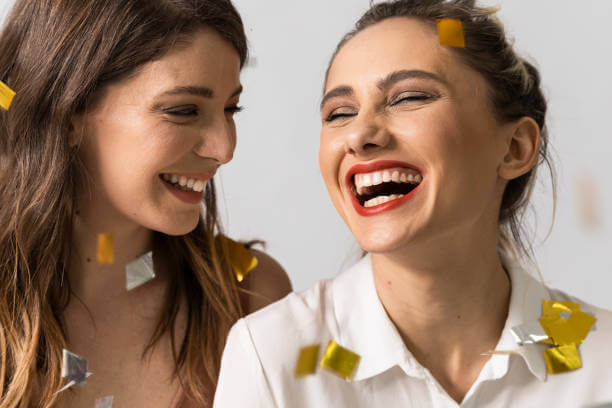 Two women smiling and laughing as gold and silver confetti falls around them