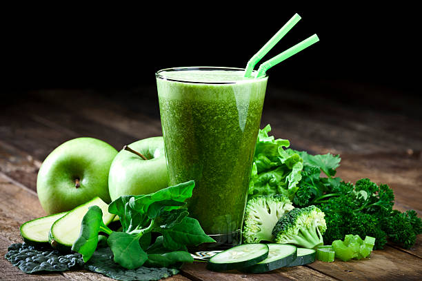 Picture of a green smoothie on a table surrounded by green fruits and vegetables.