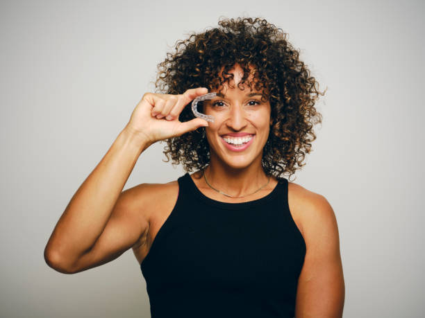 A woman in a black tank top holding up a clear tooth aligner tray