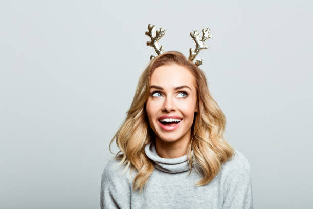 A woman smiling and wearing small sparkly antlers on her head in front of a gray background.